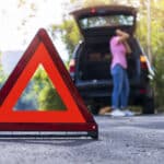 Close up red emergency stop sign standing on road. Worried and angry woman walking near his broken car talking on phone with insurance agent. Close up triangle on side road